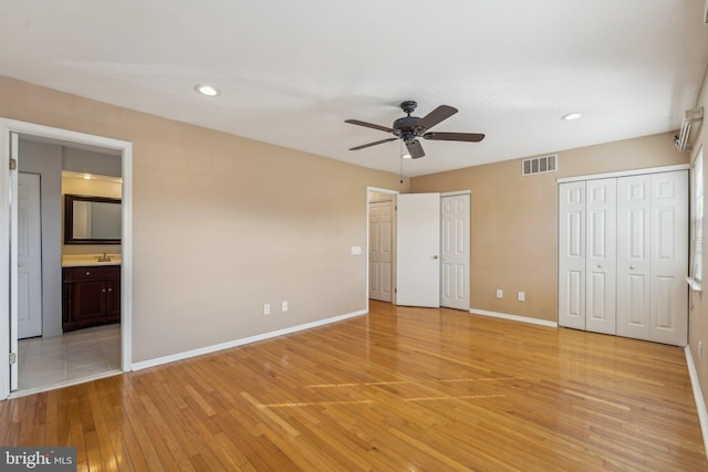 unfurnished bedroom with sink, ensuite bath, light hardwood / wood-style flooring, two closets, and ceiling fan