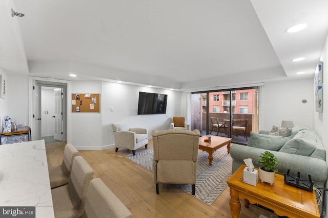 living room with a tray ceiling and light wood-type flooring