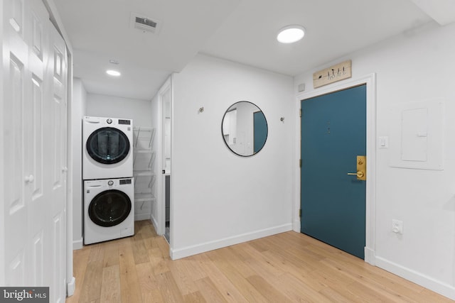 clothes washing area with stacked washer / dryer, electric panel, and light hardwood / wood-style flooring