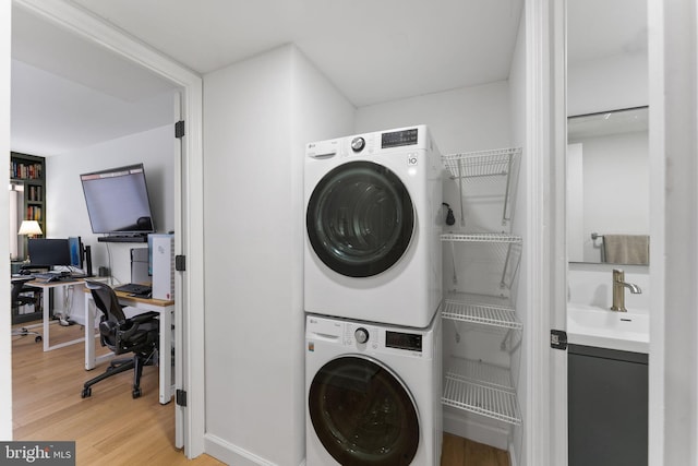 laundry room with stacked washer and dryer, light hardwood / wood-style flooring, and sink