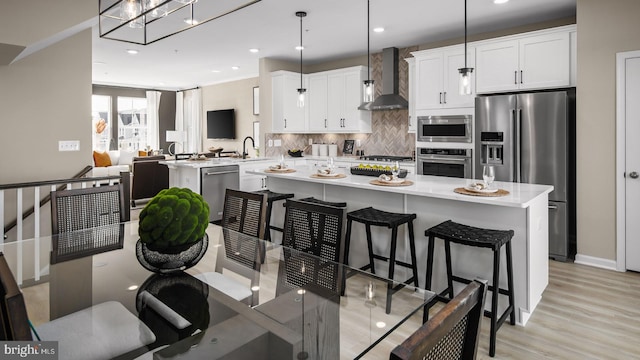 kitchen with pendant lighting, wall chimney range hood, white cabinetry, stainless steel appliances, and kitchen peninsula