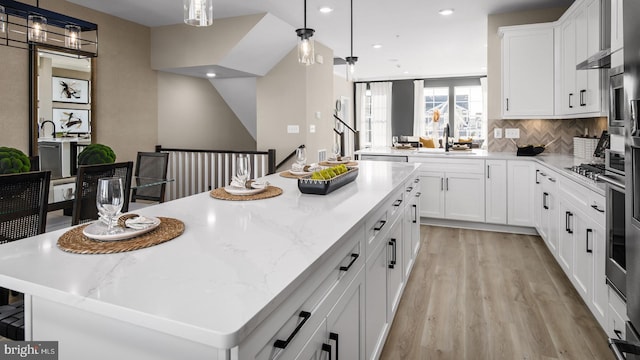 kitchen featuring sink, light hardwood / wood-style floors, white cabinets, a kitchen island, and decorative light fixtures