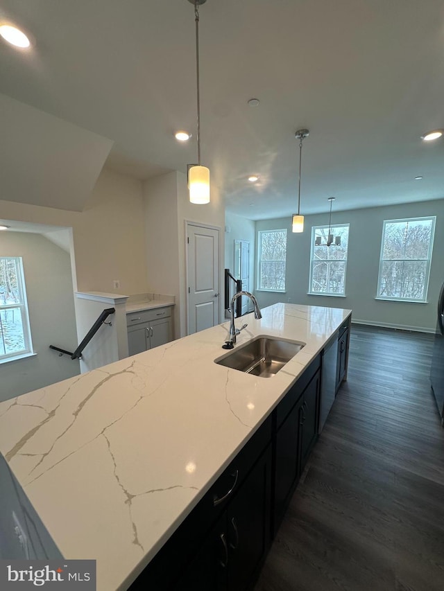 kitchen with sink, hanging light fixtures, light stone counters, an island with sink, and dark hardwood / wood-style flooring