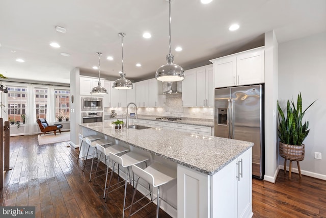 kitchen with a sink, white cabinetry, appliances with stainless steel finishes, decorative backsplash, and a center island with sink