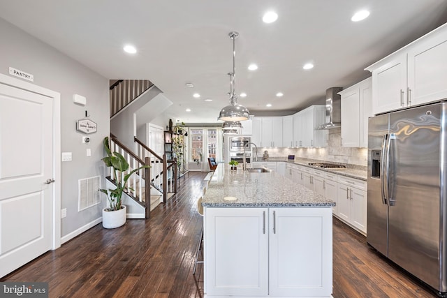 kitchen featuring visible vents, appliances with stainless steel finishes, white cabinets, a sink, and wall chimney exhaust hood