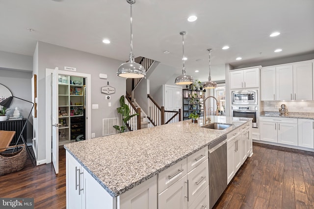 kitchen with dark wood-style flooring, stainless steel appliances, backsplash, a sink, and an island with sink