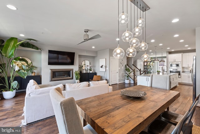 dining room with dark wood-style flooring, recessed lighting, a glass covered fireplace, ceiling fan, and stairs