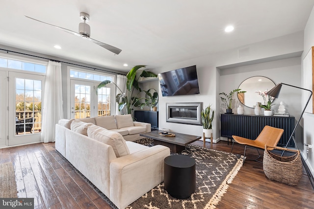 living room with dark wood-type flooring, a glass covered fireplace, visible vents, and ceiling fan