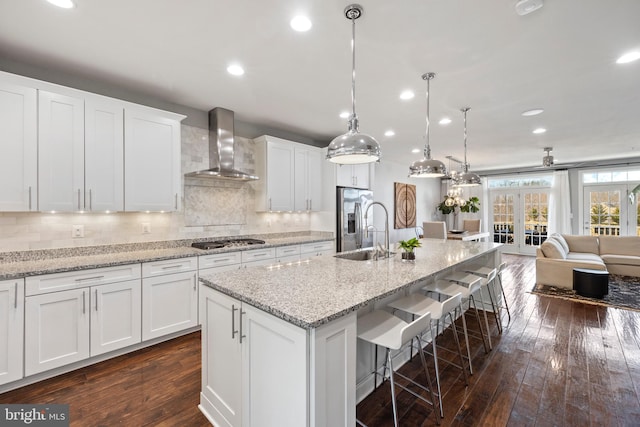 kitchen featuring wall chimney exhaust hood, a breakfast bar area, appliances with stainless steel finishes, dark wood-style flooring, and a sink