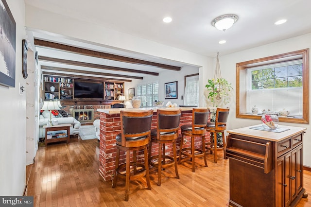 interior space featuring a brick fireplace, a center island, light hardwood / wood-style flooring, beamed ceiling, and a kitchen breakfast bar