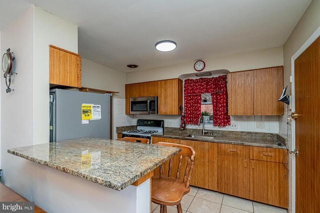 kitchen featuring appliances with stainless steel finishes, a kitchen bar, stone countertops, and sink