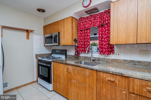 kitchen with black gas range oven, sink, decorative backsplash, dark stone counters, and light tile patterned floors