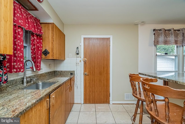 kitchen with light tile patterned flooring, stone countertops, sink, and tile walls