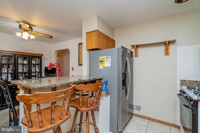 kitchen featuring stainless steel fridge with ice dispenser, a kitchen bar, dark stone counters, kitchen peninsula, and gas stove