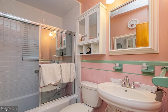 full bathroom with combined bath / shower with glass door, sink, tile walls, and toilet