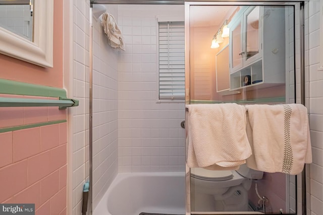 bathroom featuring tiled shower / bath, toilet, and tile walls