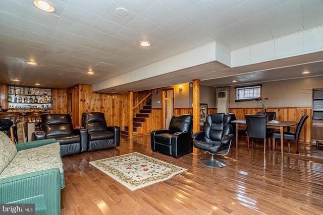 living room with hardwood / wood-style flooring, bar area, and wooden walls