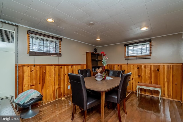 dining area with ornamental molding, wood-type flooring, and wooden walls