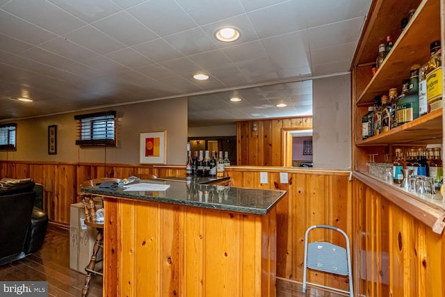 bar with dark stone counters, dark hardwood / wood-style floors, and wood walls