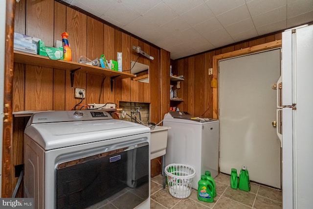 washroom featuring light tile patterned flooring, washer and clothes dryer, and wooden walls