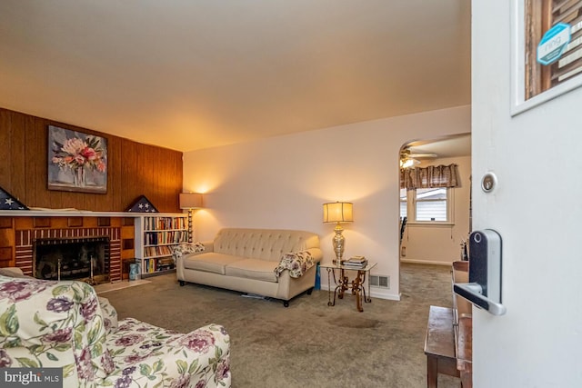 carpeted living room featuring a fireplace, ceiling fan, and wood walls