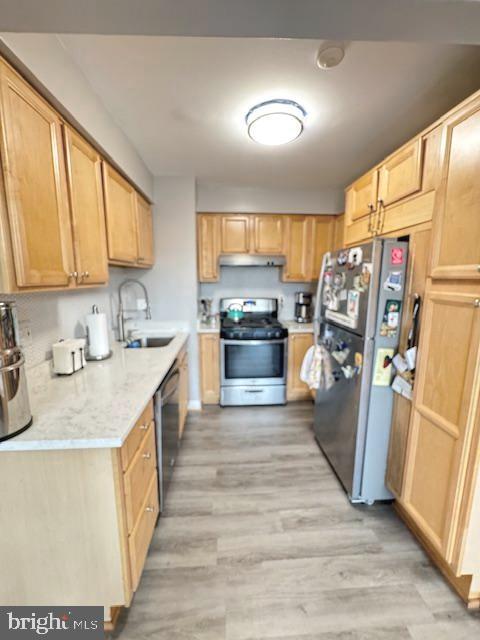 kitchen with sink, appliances with stainless steel finishes, light hardwood / wood-style floors, light stone countertops, and light brown cabinets