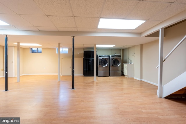 basement featuring wood-type flooring, washer and dryer, a drop ceiling, and black refrigerator with ice dispenser