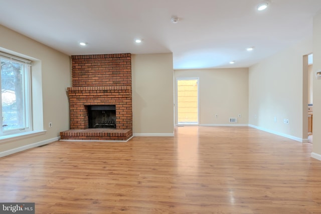 unfurnished living room featuring a brick fireplace and light wood-type flooring