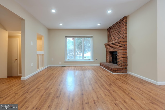 unfurnished living room featuring a brick fireplace and light hardwood / wood-style floors