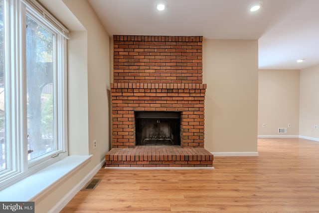 unfurnished living room with plenty of natural light, a brick fireplace, and light wood-type flooring