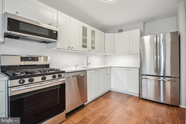 kitchen with appliances with stainless steel finishes, sink, white cabinets, and light hardwood / wood-style floors