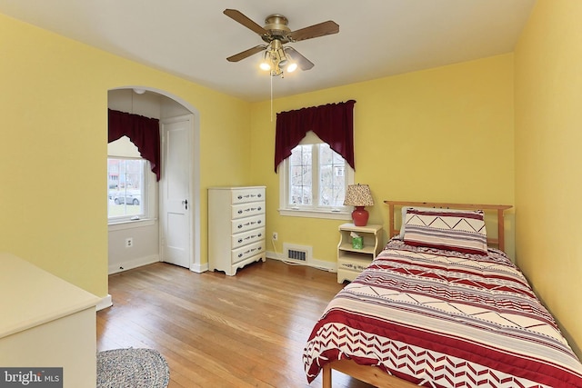 bedroom featuring hardwood / wood-style flooring, multiple windows, arched walkways, and visible vents