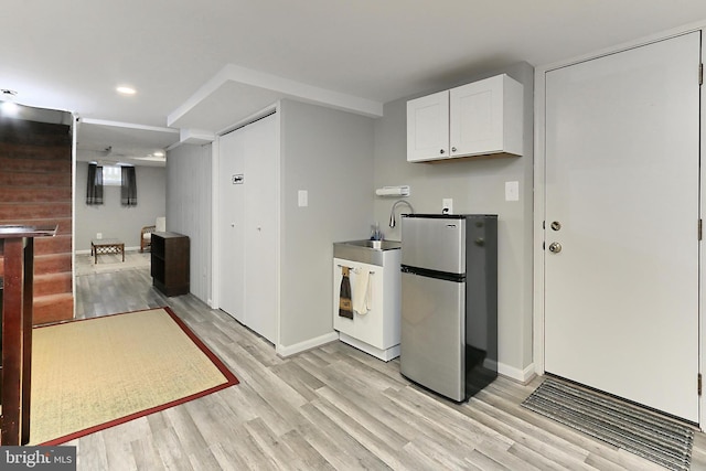 kitchen featuring baseboards, light wood-type flooring, freestanding refrigerator, white cabinets, and a sink