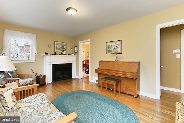 living area featuring visible vents, a fireplace with flush hearth, baseboards, and wood finished floors