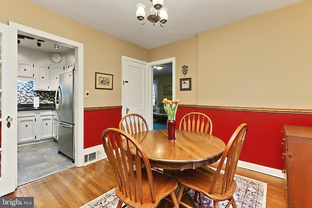 dining space featuring a notable chandelier, baseboards, visible vents, and wood finished floors