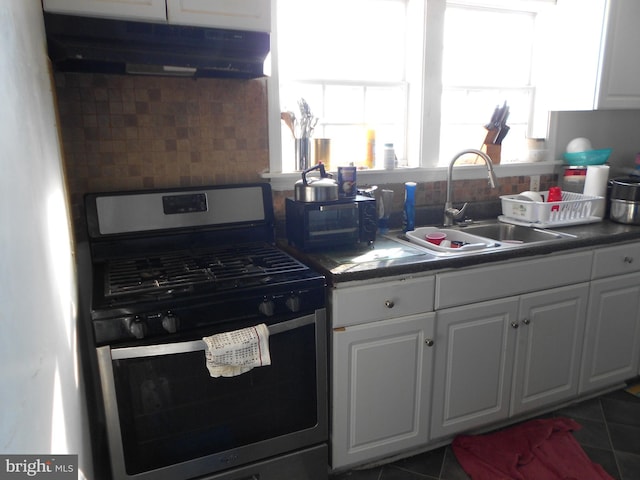 kitchen featuring stainless steel gas stove, tasteful backsplash, white cabinetry, sink, and dark tile patterned floors