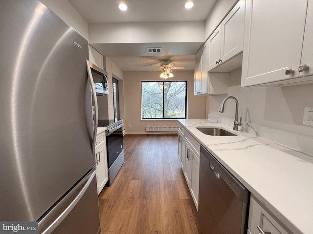 kitchen with sink, appliances with stainless steel finishes, white cabinetry, light stone countertops, and light hardwood / wood-style floors