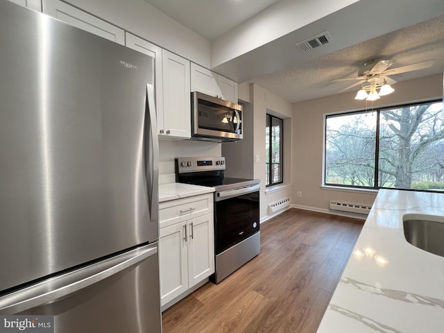 kitchen featuring stainless steel appliances, light stone countertops, a textured ceiling, white cabinets, and light wood-type flooring