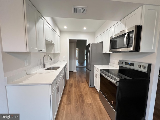 kitchen with light hardwood / wood-style floors, white cabinets, and appliances with stainless steel finishes