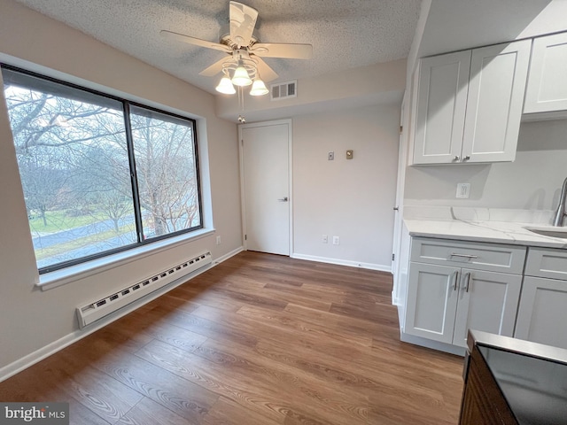 unfurnished dining area with sink, a textured ceiling, a baseboard radiator, ceiling fan, and light hardwood / wood-style floors