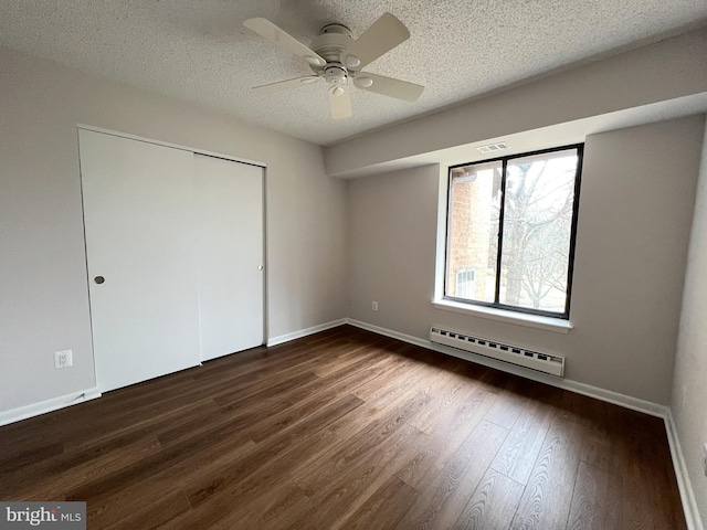 unfurnished bedroom with dark hardwood / wood-style flooring, a baseboard heating unit, ceiling fan, a textured ceiling, and a closet