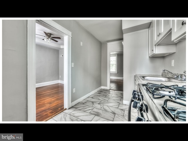 kitchen featuring white cabinetry, ceiling fan, stainless steel range with gas stovetop, and sink