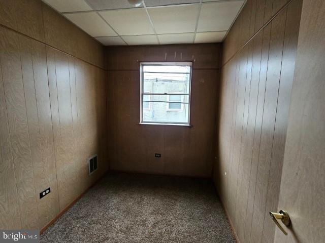 carpeted spare room featuring a drop ceiling and wooden walls