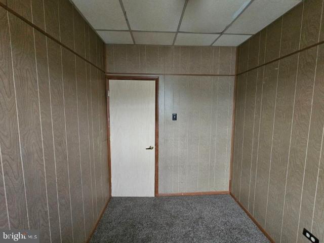 empty room with a drop ceiling, carpet, and wood walls