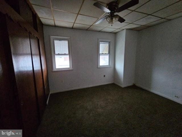 empty room featuring a drop ceiling, ceiling fan, and dark colored carpet