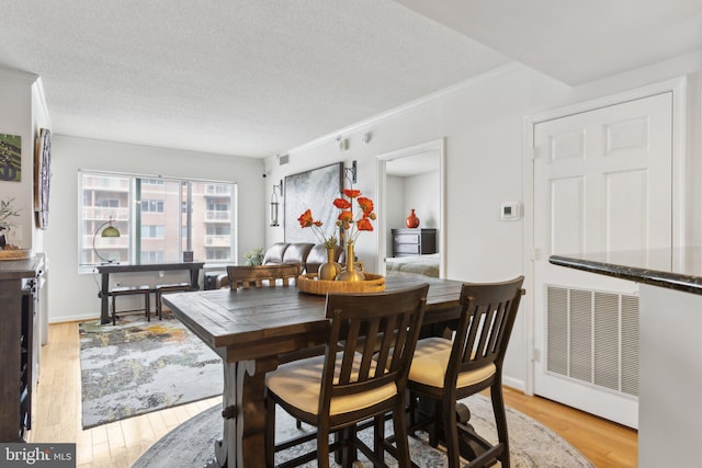 dining room with ornamental molding, a textured ceiling, and light wood-type flooring