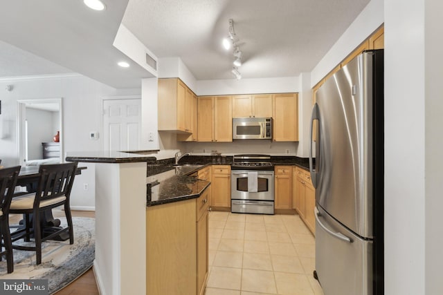 kitchen with light tile patterned flooring, sink, dark stone counters, kitchen peninsula, and stainless steel appliances