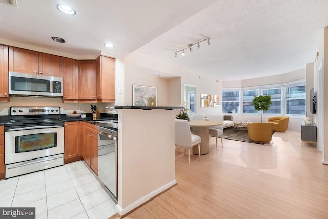 kitchen with open floor plan, stainless steel appliances, brown cabinetry, and dark countertops