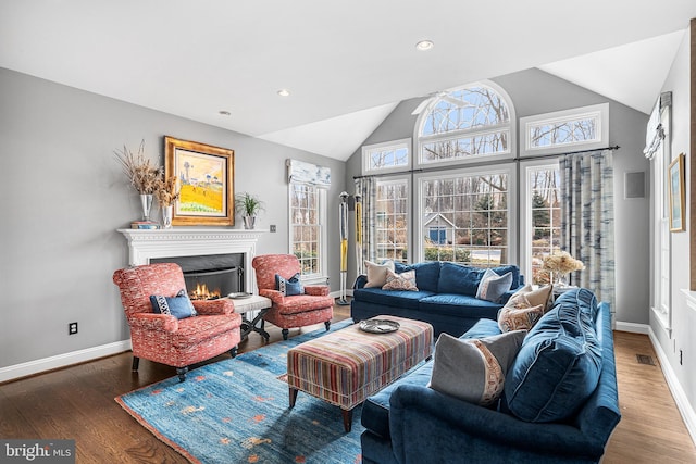 living room with a warm lit fireplace, visible vents, vaulted ceiling, and wood finished floors