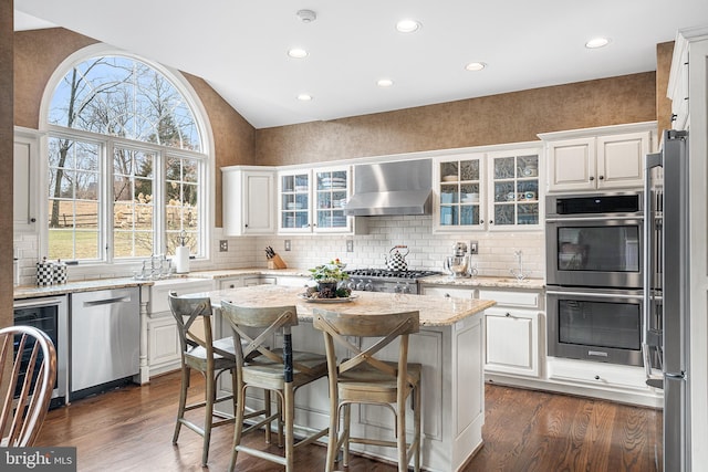 kitchen with stainless steel appliances, dark wood-type flooring, white cabinetry, wall chimney exhaust hood, and plenty of natural light